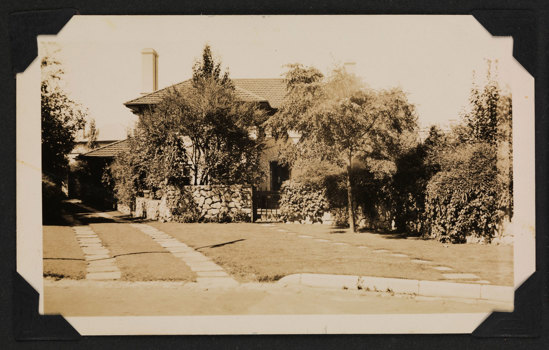 Large house viewed from the street. There is a driveway and tall trees in the front