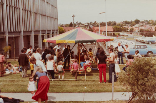 Numerous children and adults standing infront of small carousel