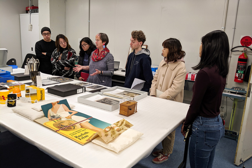 Group of men and women standing around a white-topped table with photographic objects on it