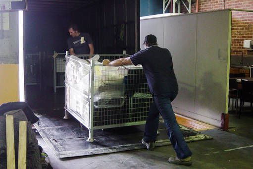 Two men with a metal pallet cage of items on the tailgate of a removal truck