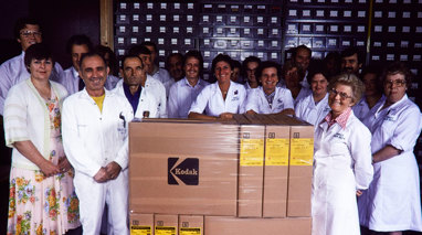 Group of staff in white lab coats standing with boxes on a pallet