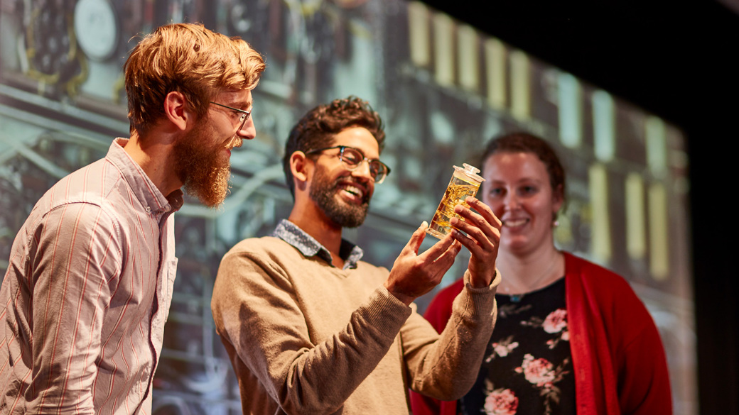 Three people looking at a specimen of a animal in a jar