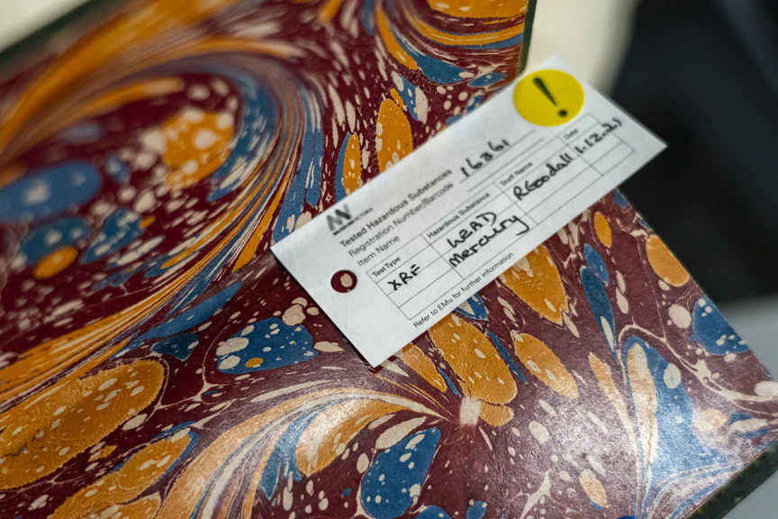 A close up image of a speckled red yellow and blue page in a book. A warning label states that is contains lead and mercury. 