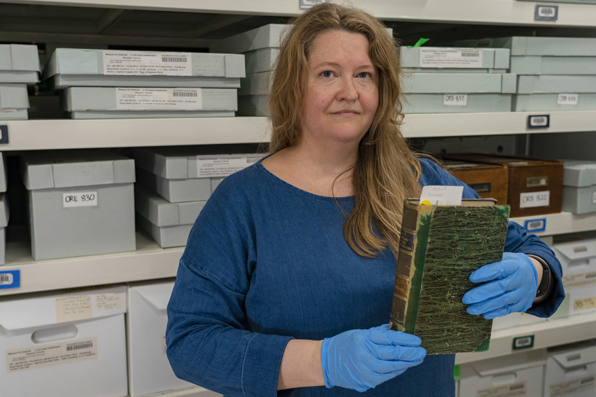 a woman wearing a blue top and gloves holds a green book