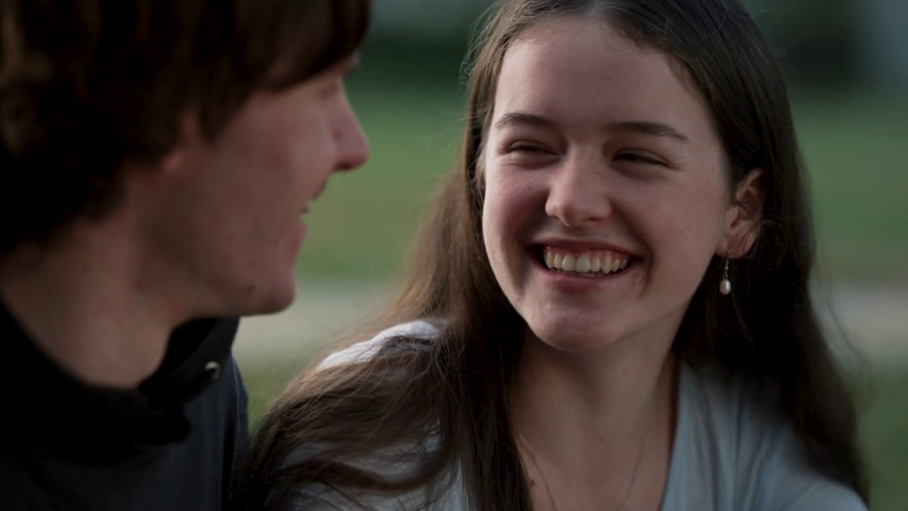 A close-up image shows two people looking at each other and smiling. One of the people is in focus; they have long brown hair and wear a pearl earring.