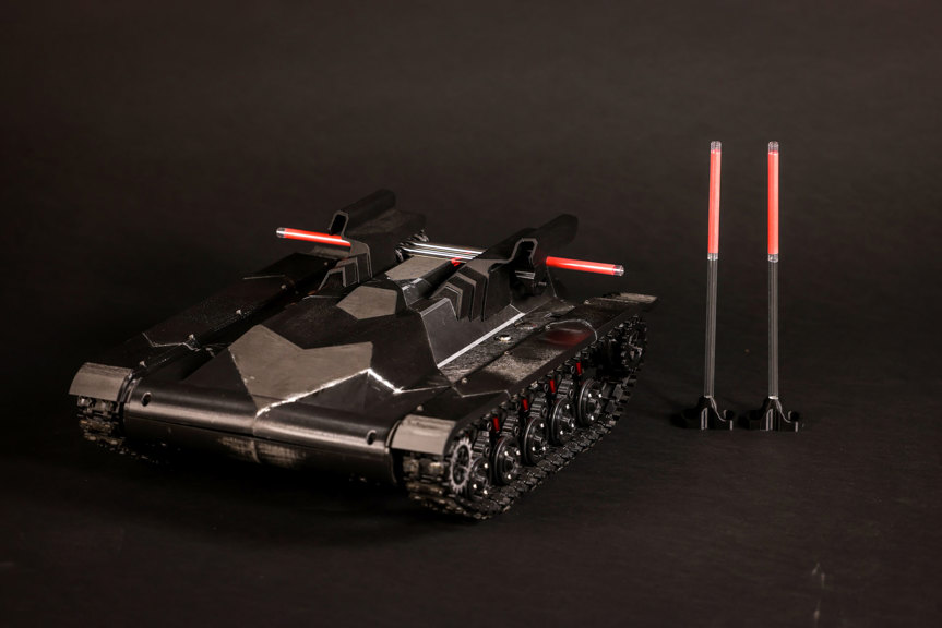 A photograph of a black system, with tank-like wheels, sitting next to two upright red lights.