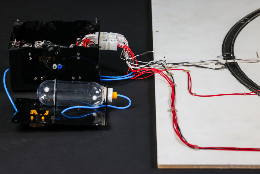 A close-up photo of system components, showing several red, blue, and white wires connected to a plastic bottle and a curved track.