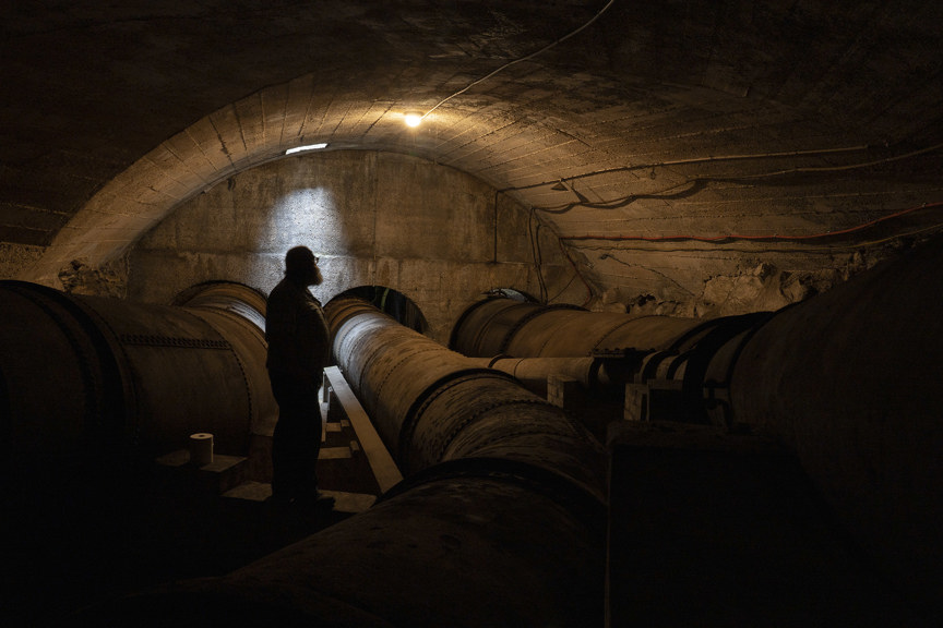a photograph of a man silhouetted in a tunnel with three large pipes 