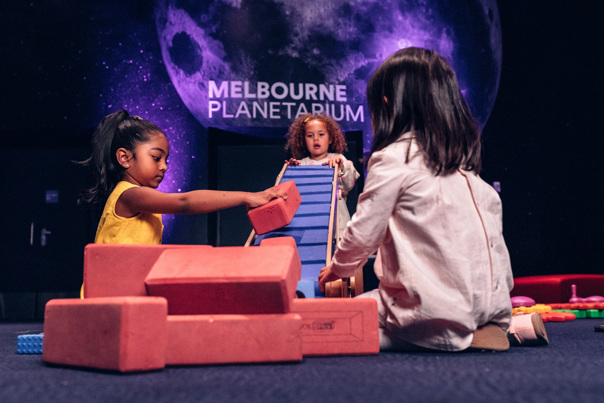 Three children, 3-5 years old, play together with foam kick bricks and a conveyor belt in the Tiny Tinkerers space at Scienceworks' Little Kids' Day In.