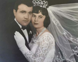 Man in suit embraced by woman wearing tiara and veil.