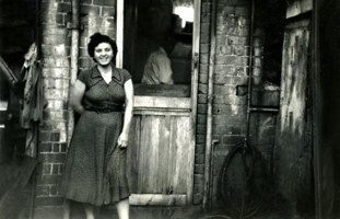 A woman stands by a door with a man is inside.