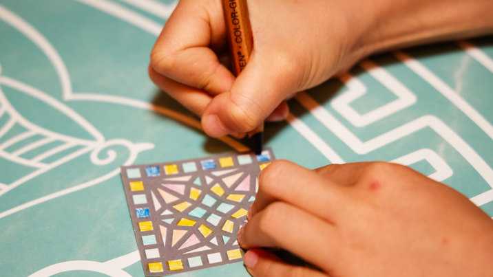 Close up shot of two hands holding a pencil and colouring a mosaic design