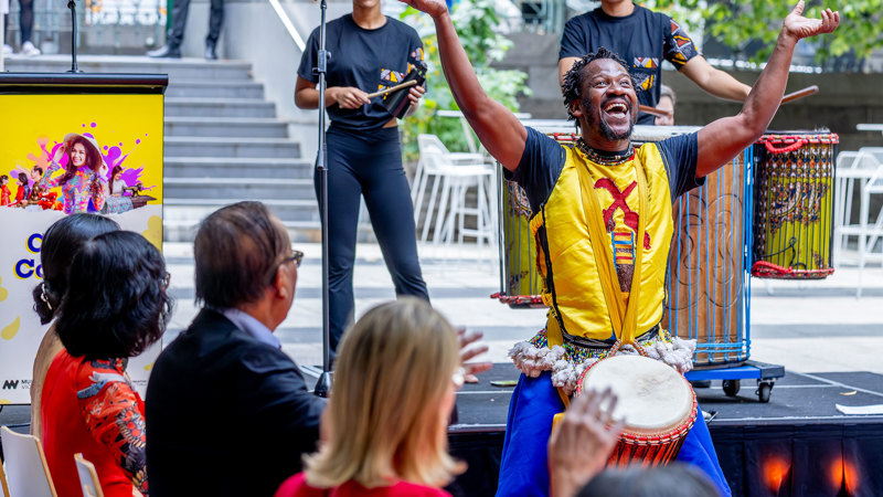 A man with his arms raised in the air performing at Immigration Museum.