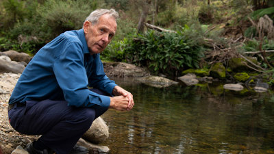 Bob brown crouching beside a river.