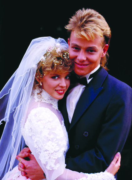A young man and woman, in wedding attire, hug while posing for a photo