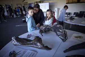 Adults and children touching large dinosaur bones on a table