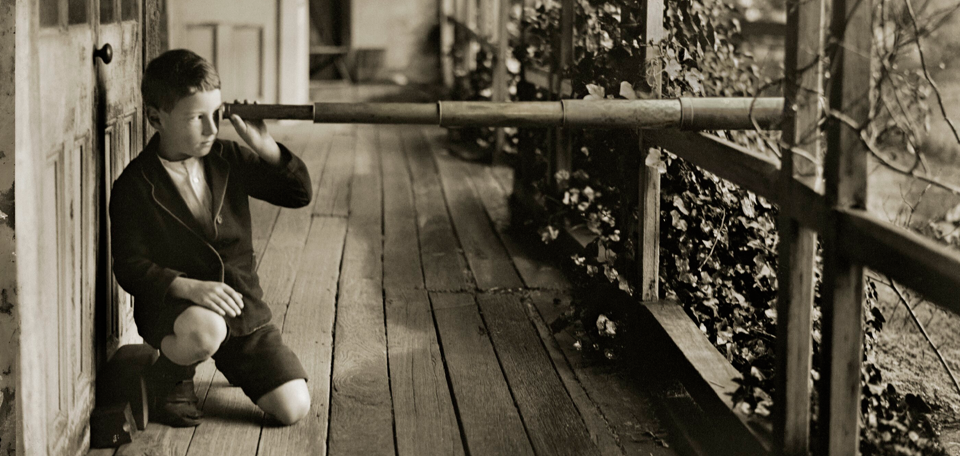 Boy on a wooden verandah looking through a telescope.
