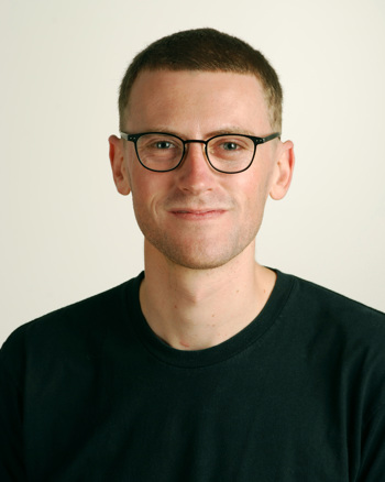 Head and upper torso of a bespectacled man in black