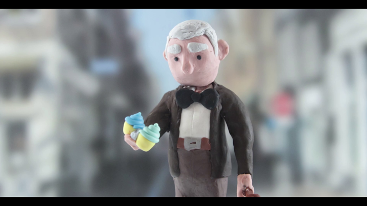 A clay figurine of an elderly man holding two cupcakes.