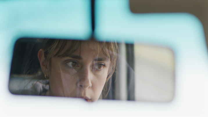 A reflection of a woman in the windscreen mirror of a car.