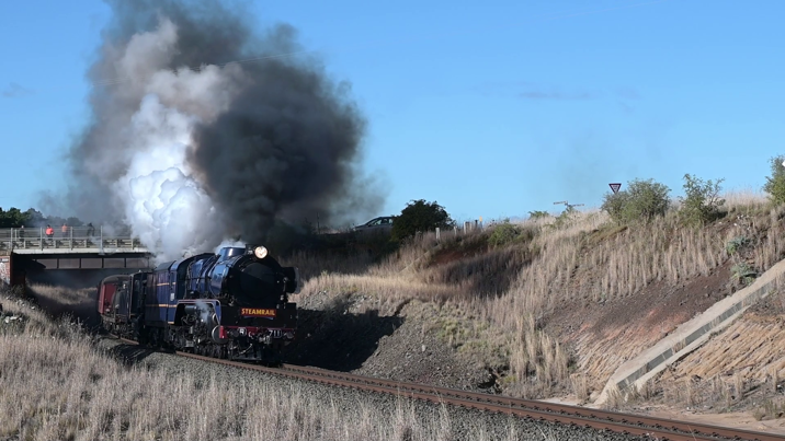 A steam train blowing out smoke whilst passing under a bridge.