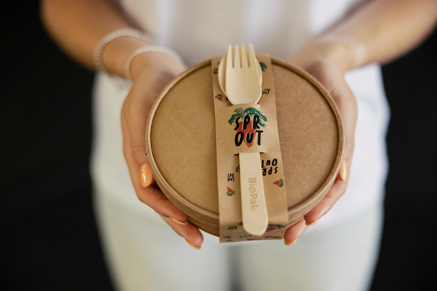 A person holding a takeaway bowl and a set of BioPak cutlery. The packaging is branded with a logo reading ‘Sprout’.