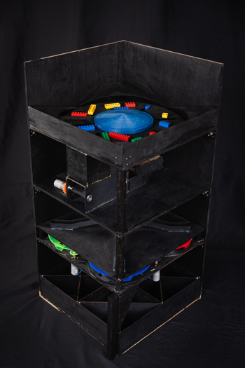 The photo shows a tall, rectangular black system with four layers. Red, blue, yellow, and green LEGO pieces are sitting on top.