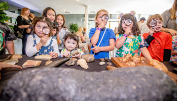 Young visitors use a magnifying glasses to look at fossils on a table.