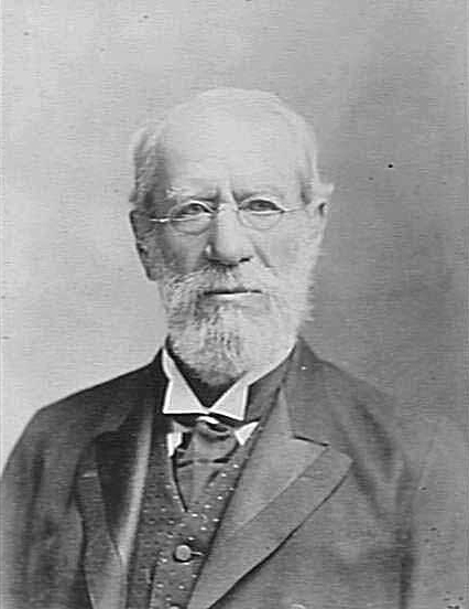 Photographic portrait of a bearded, bespectacled man in a suit