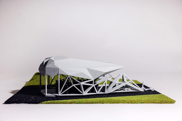 Architectural model featuring a faceted grey roof supported by white geometric structural framework, on a base of artificial turf.