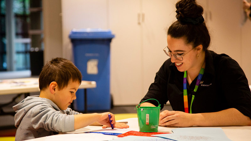 A child is supervised by a visitor engagement officer while they participate in a craft activity.