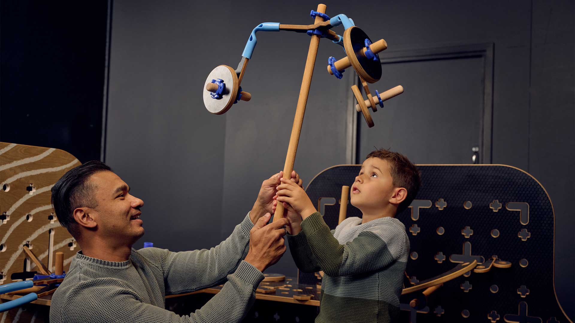 A man and a boy hold up a wood and plastic contraption they built in Tinkertown 