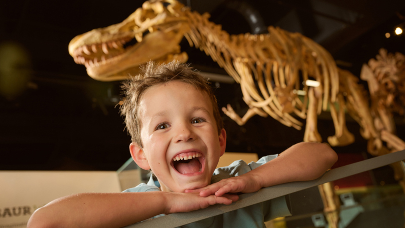  Child smiling in Dinosaur Walk exhibition during the Tiny Tours event.