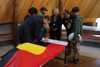 Man signing documents. Five people look on.