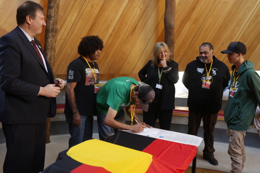 Man signing documents. Five people looking on.