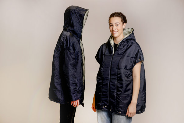 Two models wearing navy blue, oversized hooded puffer jackets with grey lining, one sleeveless and the other with sleeves, against a neutral background.