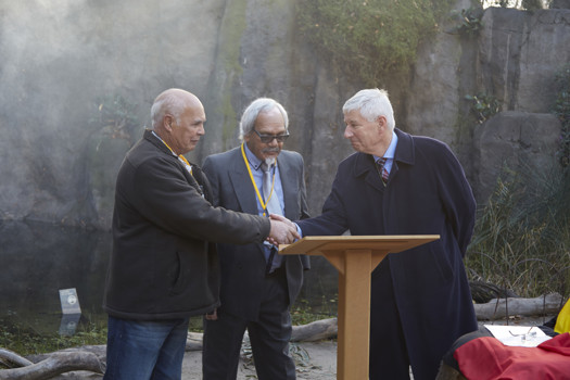 Two men shaking hands. On man looking on.