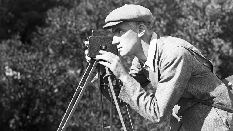 Black and white photograph of a man looking through a movie camera