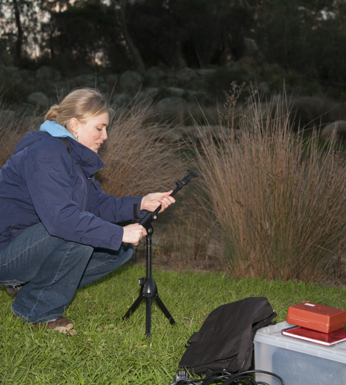 Phd Biology student, Katie Smith, recording frog calls beside a lake in a wetland environment at dusk.