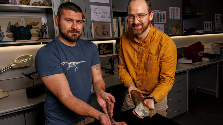Two men looking towards the camera each holding a fossils