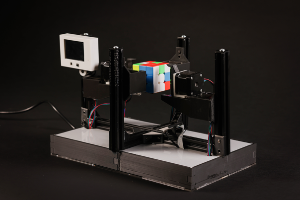 A Rubik’s Cube held up by black stepper motors affixed to a silver rectangular base.