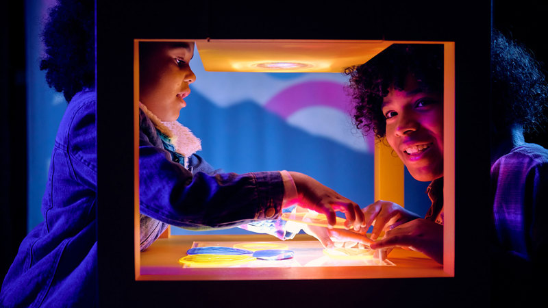 Two children moving transparent coloured shapes over each other to create different colours in Colour exhibition at Scienceworks.