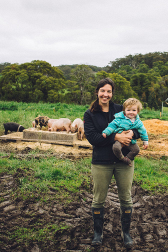 Woman holding a toddler with pigs at a trough in the background