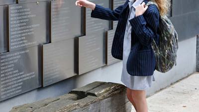  A student in uniform carrying a backpack viewing the memorial wall in the Tribute Garden at Immigration Museum