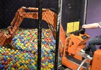 A child operating a bulldozer which is picking up plastic balls from an enclosed cage