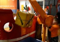A child using a crane to move a box labelled 'clothing'