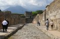 Visitors walking down a Pompeii street, at the end of which stands the Tower of Mercury. Vesuvius is in the background.