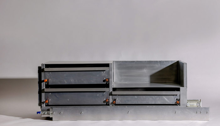 Grey metal slide-out cooking system with multiple compartments featuring orange handles, drawer sections, and mounting hardware.