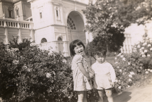 Two children near rose bushes outside partially visible building.