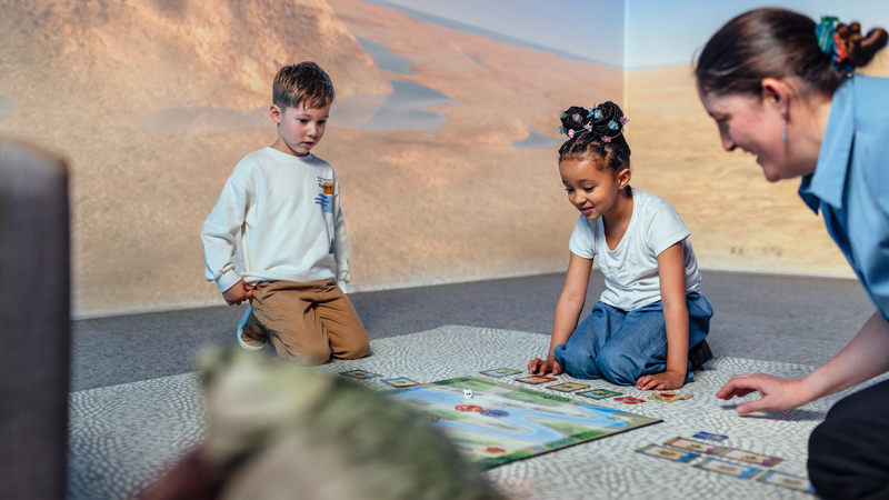 A teacher and two young children playing a board game.